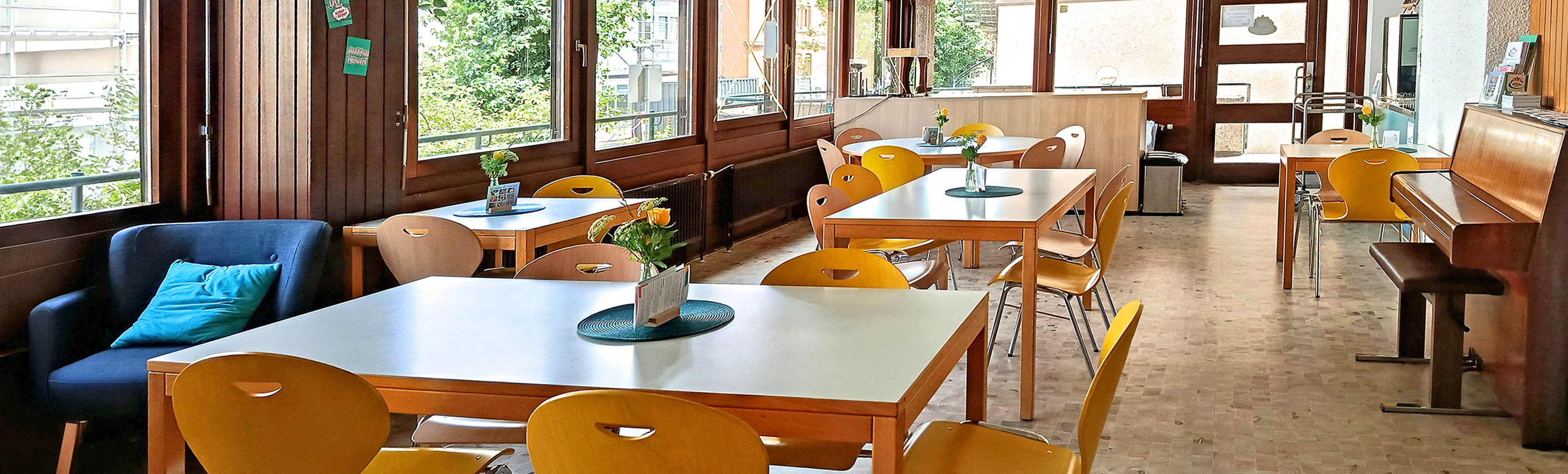 Ein großer Raum mit Theke, Esstischen und Stühlen, weiteren Sitzecken und einer großen Spielelecke für Kinder.
